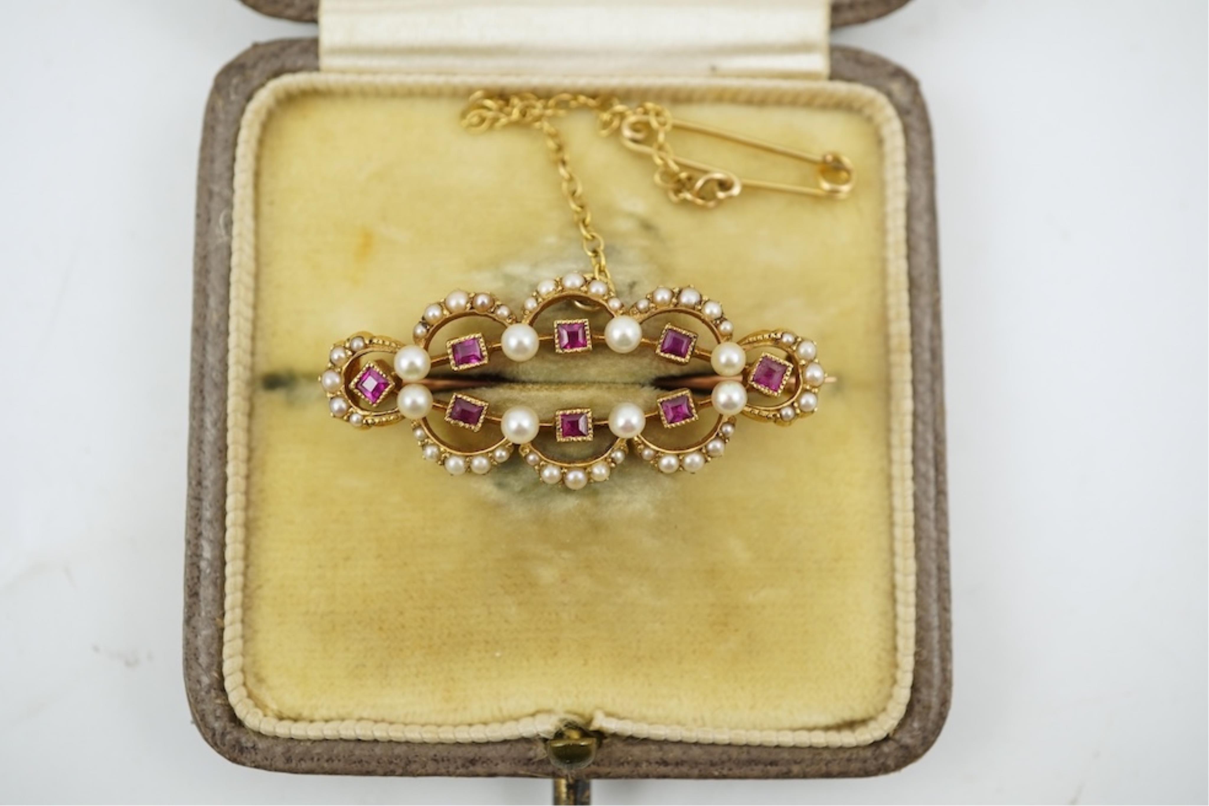 An Edwardian 15ct, ruby and seed pearl cluster set brooch, 33mm, with safety chain, gross weight 4.1 grams.